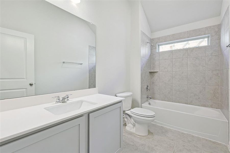 Full bathroom with tile patterned floors, vanity, tiled shower / bath combo, and toilet