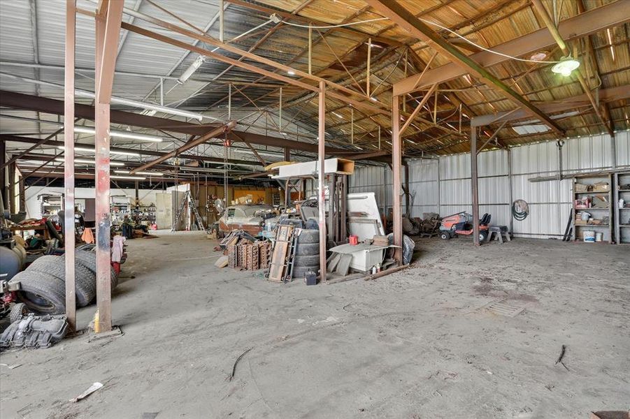 Spacious  garage featuring a high ceiling, exposed metal beam construction, corrugated metal wall panels, and a concrete floor