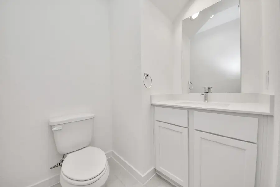 Sophisticated half bathroom adorned with contemporary finishes. The elegant 5-panel door welcomes you to a space where style meets functionality. Notice the sleek hardware accents that add a touch of modern charm. The vanity boasts light-colored countertops, beautifully complemented by a tasteful vanity light, creating a well-lit and inviting atmosphere.