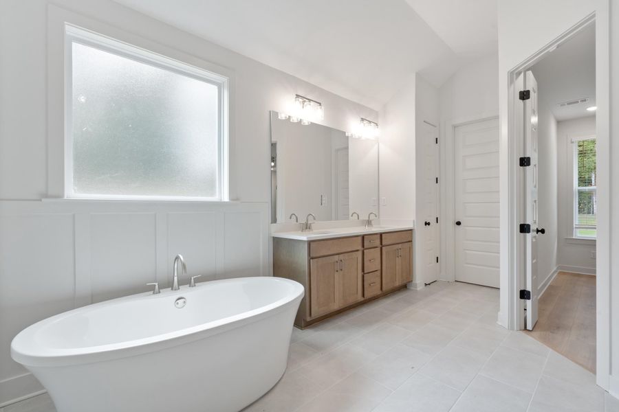 Freestanding soaking tub, dual vanity with wood-finish cabinetry, sleek white countertop, and tiled flooring Freestanding soaking tub, dual vanity with wood-finish cabinetry, sleek white countertop, and tiled flooring