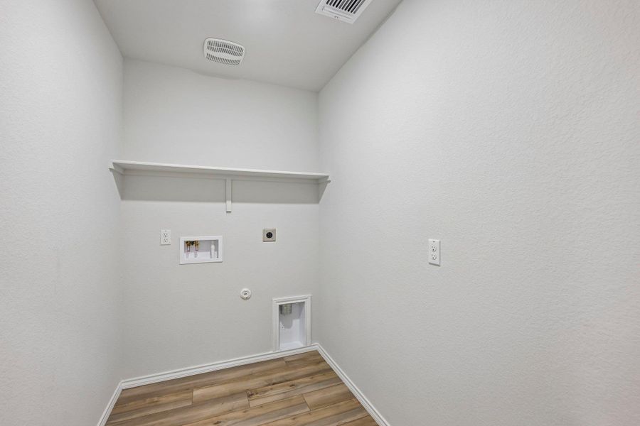 Dedicated utility space featuring wood-finish flooring, a built-in shelf, and essential appliance hookups