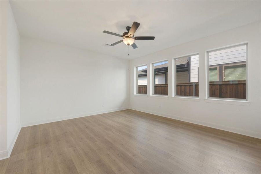 Spacious room with light wood-finish flooring, crisp white walls, and a contemporary ceiling fan with integrated lighting
