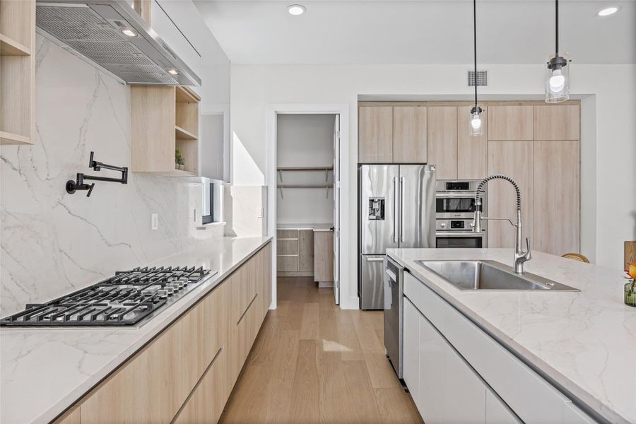 Kitchen with light stone counters, extractor fan, decorative light fixtures, light wood-style floors, and stainless steel appliances
