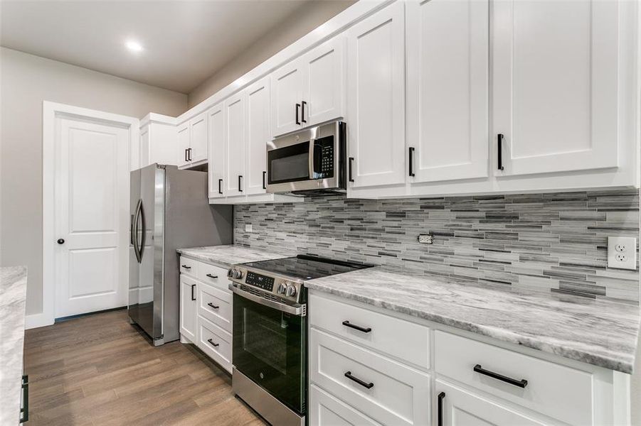 Kitchen with appliances with stainless steel finishes, white cabinetry, light stone countertops, dark wood-type flooring, and recessed lighting