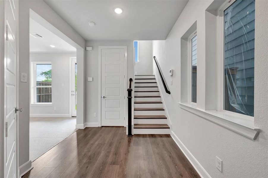 Entryway featuring wood-finish flooring, white paneled doors, and a staircase with a dark wood handrail and baluster