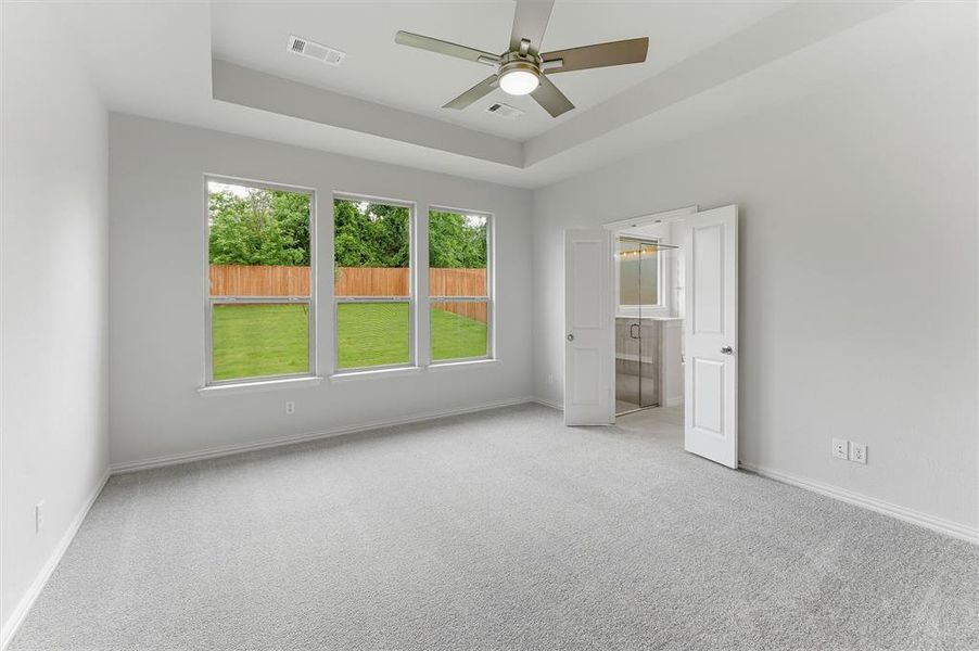 Spacious room featuring light gray carpeting, a tray ceiling, and a ceiling fan with integrated lighting