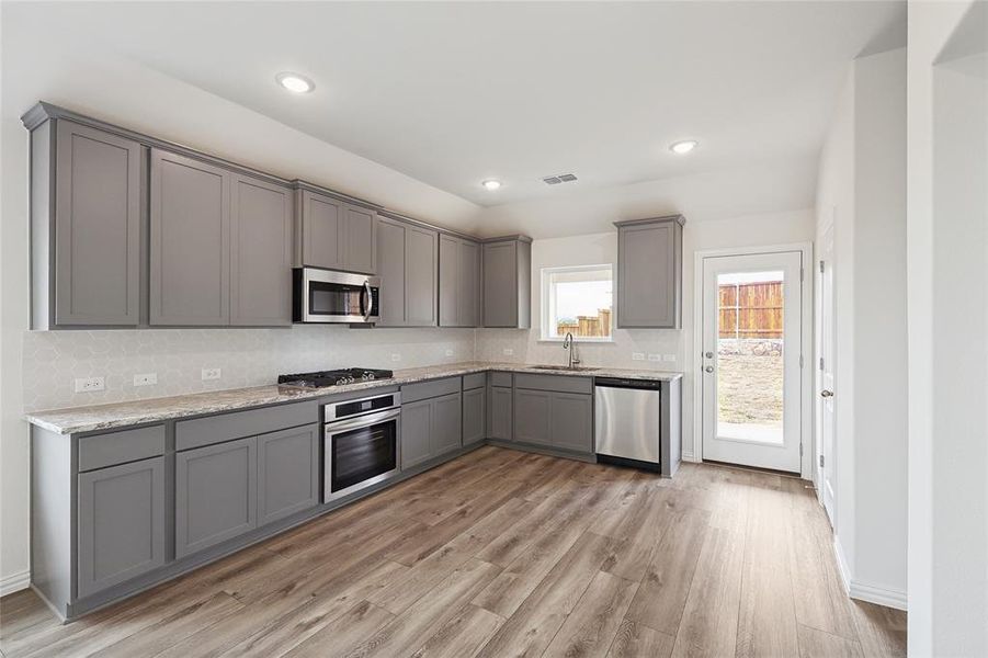 Kitchen featuring stainless steel appliances, gray cabinets, light wood-type flooring, light stone counters, and recessed lighting
