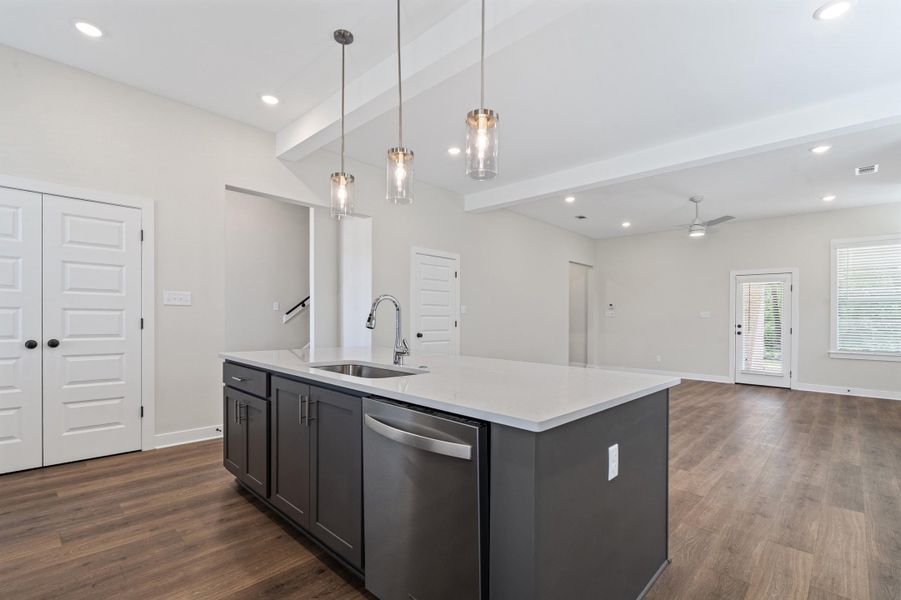 Kitchen featuring open floor plan, stainless steel dishwasher, light stone countertops, an island with sink, and pendant lighting Kitchen featuring open floor plan, stainless steel dishwasher, light stone countertops, an island with sink, and pendant lighting