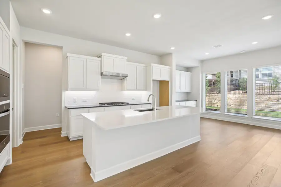 Kitchen featuring white cabinets, decorative backsplash, light wood-style flooring, recessed lighting, and a kitchen island with sink