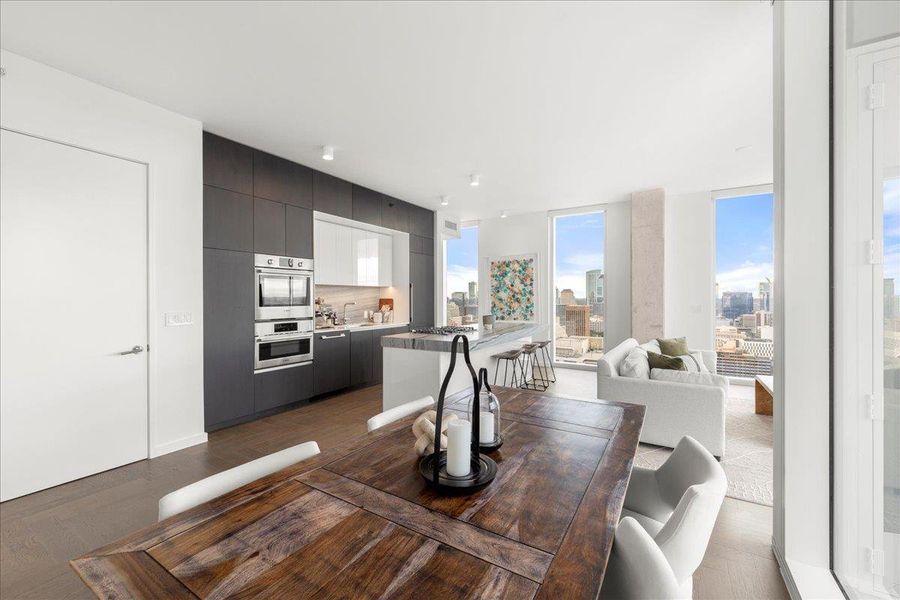 Dining area with floor-to-ceiling glass opens to the chef’s kitchen, featuring upgraded Fantasy Ocean marble countertops and a full Bosch appliance suite.