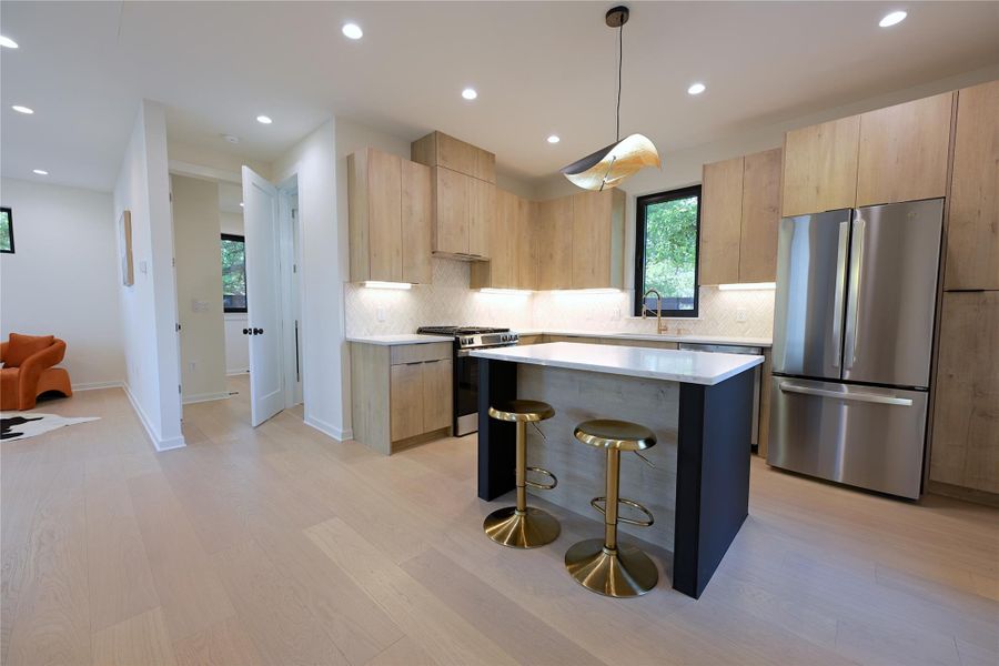 The kitchen features light wood European style cabinetry, stainless steel appliances, a center island with seating, and recessed lighting