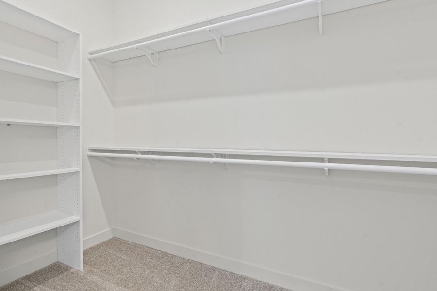 Walk-in closet featuring built-in shelving, two hanging rods, a single top shelf, white painted walls, and light-colored carpet flooring