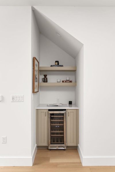 Indoor dry bar with wine cooler, open shelves, light wood-style floors, and vaulted ceiling