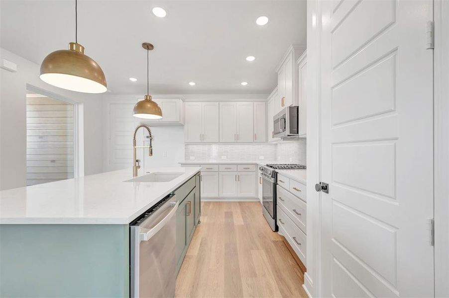 Kitchen featuring a large island with a built-in sink and dishwasher, light-toned wood-finish flooring, recessed lighting, and a subway tile backsplash