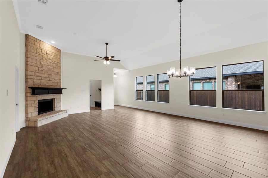 Spacious living area featuring a stone-clad fireplace with a dark wood mantel, wood-finish flooring, and vaulted ceilings