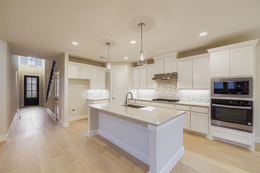 Kitchen featuring backsplash, stainless steel appliances, white cabinetry, light wood-type flooring, and recessed lighting Kitchen featuring backsplash, stainless steel appliances, white cabinetry, light wood-type flooring, and recessed lighting