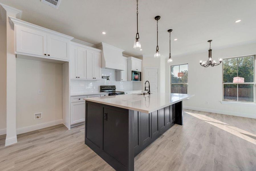 Kitchen with a center island with sink, white cabinetry, stainless steel electric stove, and decorative light fixtures