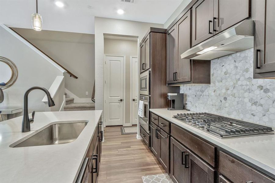 Kitchen featuring decorative light fixtures, light hardwood / wood-style flooring, backsplash, stainless steel appliances, and sink