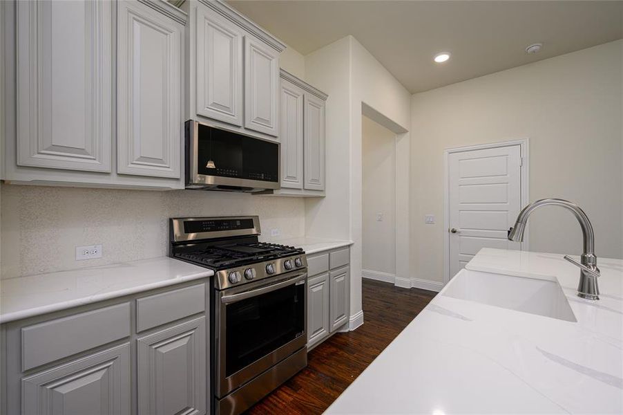Kitchen featuring a farm house sink, light stone countertops,  appliances with stainless steel finishes, and gray cabinetry