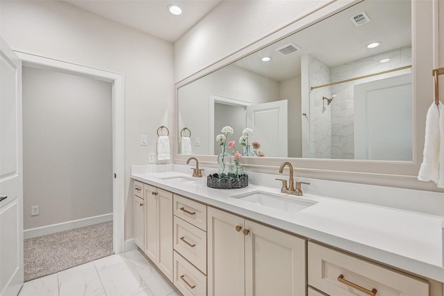 Accessible directly from the adjoining bedroom as well as the upstairs hallway, this full bath features a long dual-sink vanity with abundant cabinetry, oversized mirror, brushed-gold fixtures and a separate tub/shower area.