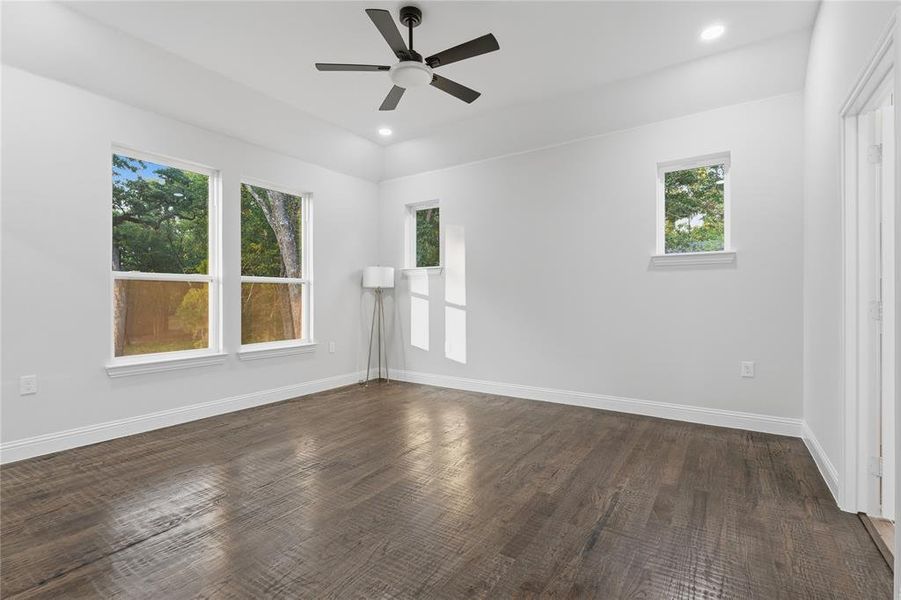 Spacious room featuring wood-finish flooring, white walls, and multiple windows Spacious room featuring wood-finish flooring, white walls, and multiple windows