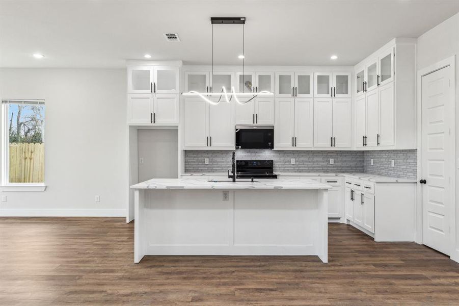 Kitchen featuring light stone countertops, white cabinets, a center island with sink, and decorative light fixtures