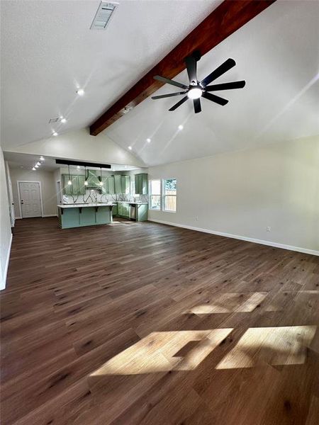 Expansive open-concept living area featuring high vaulted ceilings with exposed wood beams and recessed lighting