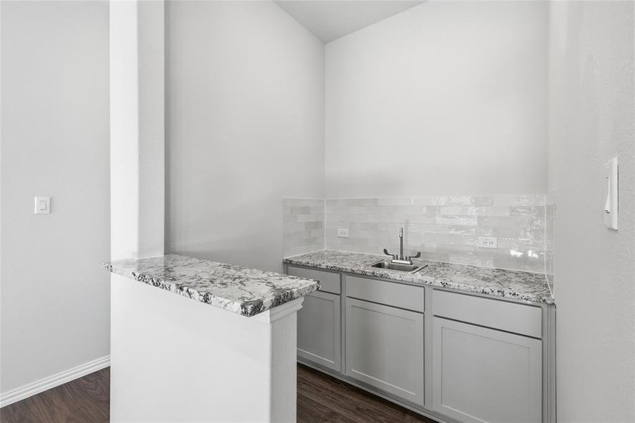 Kitchen featuring a peninsula, dark wood-type flooring, gray cabinetry, and light stone countertops Kitchen featuring a peninsula, dark wood-type flooring, gray cabinetry, and light stone countertops