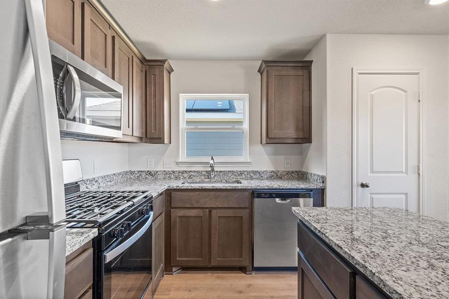 Kitchen featuring stainless steel appliances, a sink, a textured ceiling, light stone countertops, and light wood-type flooring