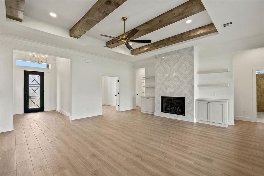 Unfurnished living room with a premium fireplace, a ceiling fan, light wood finished floors, beamed ceiling, and recessed lighting Unfurnished living room with a premium fireplace, a ceiling fan, light wood finished floors, beamed ceiling, and recessed lighting