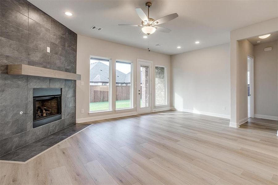 Unfurnished living room featuring ceiling fan, light wood-type flooring, tile walls, and a tile fireplace