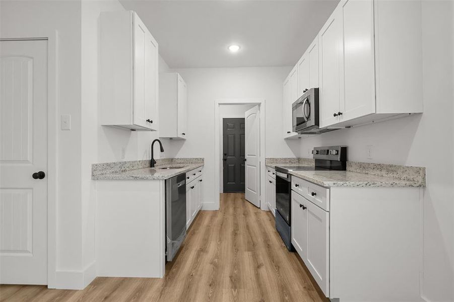 Kitchen featuring light stone countertops, sink, white cabinetry, and appliances with stainless steel finishes