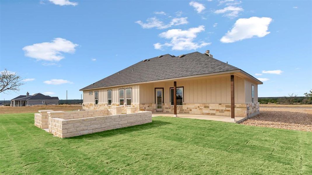 A spacious grassy lawn extends from the covered back patio and stone-accented exterior wall. A spacious grassy lawn extends from the covered back patio and stone-accented exterior wall.