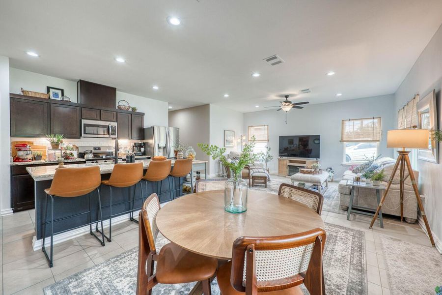 Open-concept living space featuring a central kitchen island with seating, dark wood cabinetry, stainless steel appliances, and recessed lighting