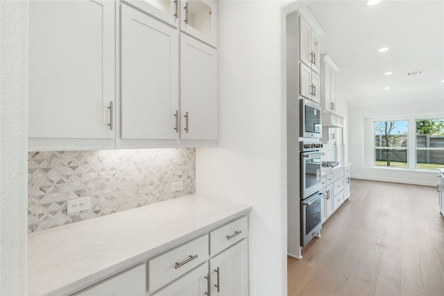 Kitchen with white shaker cabinets, geometric tile backsplash, quartz countertops, and stainless steel appliances on wood floors.