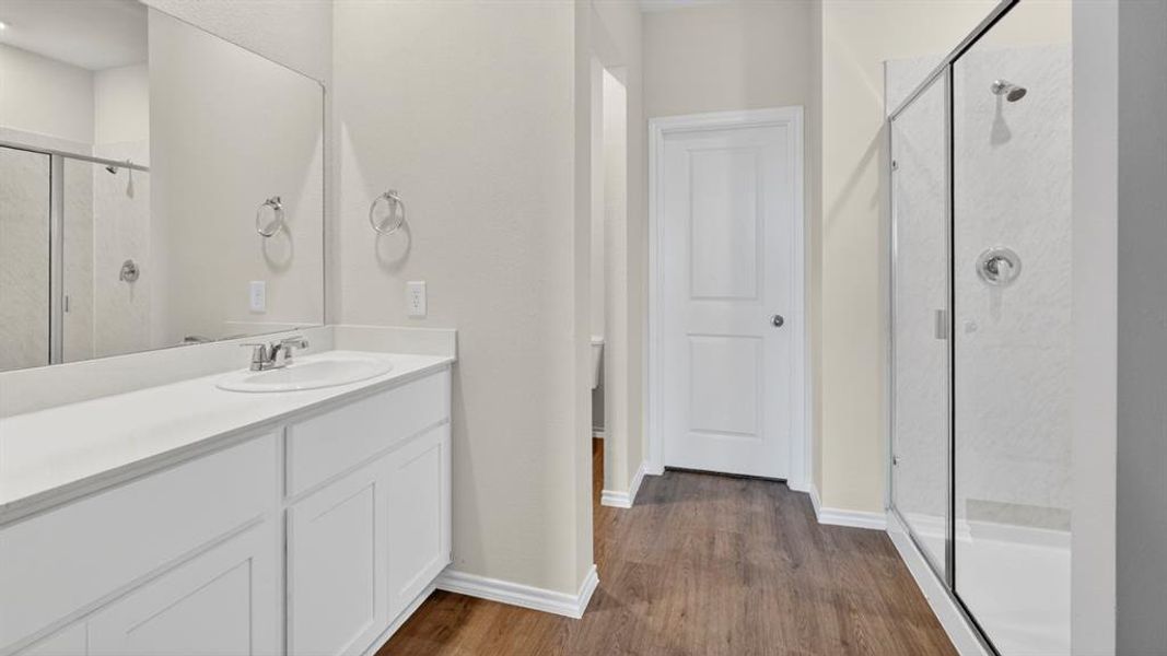 Bathroom featuring a glass-enclosed shower, white vanity with integrated sink, chrome fixtures, wood-finish flooring, and a large wall mirror