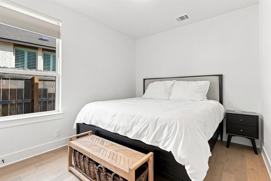 Warm hardwood floors and a large window create a serene atmosphere in this bedroom.