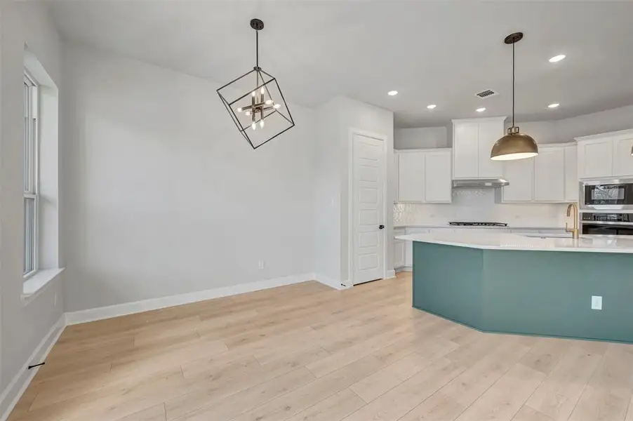 Kitchen with white cabinetry, hanging lights, light wood-type flooring, and stainless steel appliances Kitchen with white cabinetry, hanging lights, light wood-type flooring, and stainless steel appliances