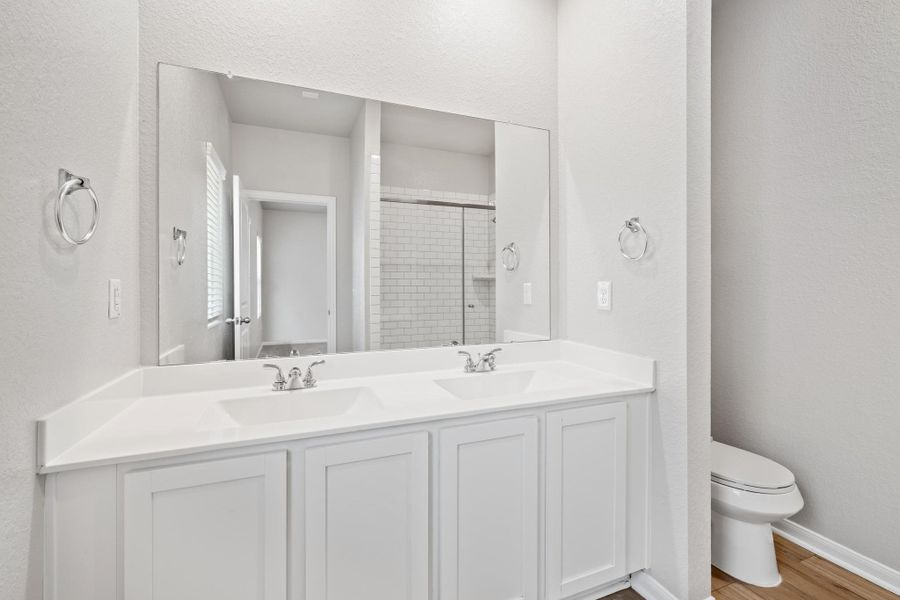 Bathroom with a textured wall, double vanity, a tile shower, and wood finished floors Bathroom with a textured wall, double vanity, a tile shower, and wood finished floors