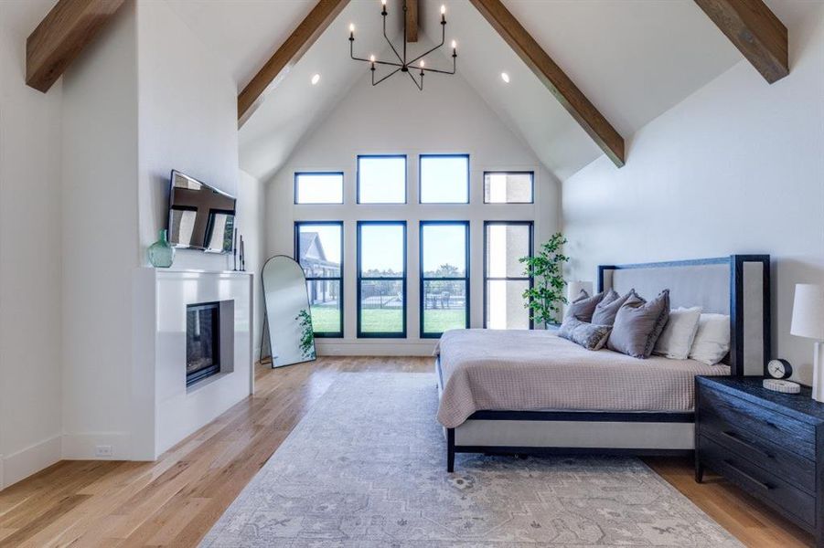 Bedroom featuring beamed ceiling, a chandelier, high vaulted ceiling, light wood-type flooring, and a glass covered fireplace Bedroom featuring beamed ceiling, a chandelier, high vaulted ceiling, light wood-type flooring, and a glass covered fireplace