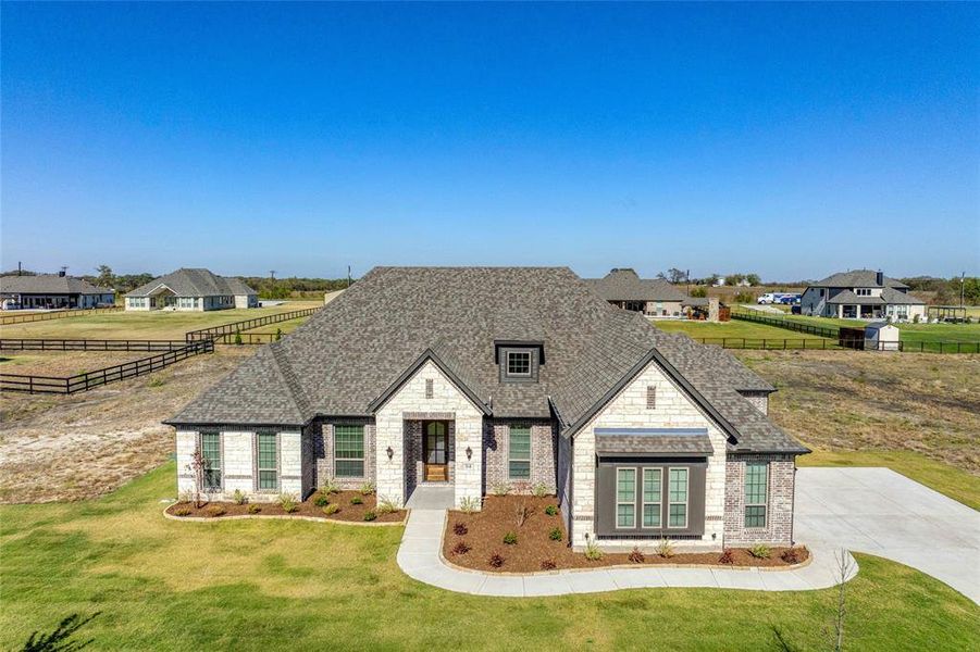 French country home with stone siding, roof with shingles, brick siding, and a residential view