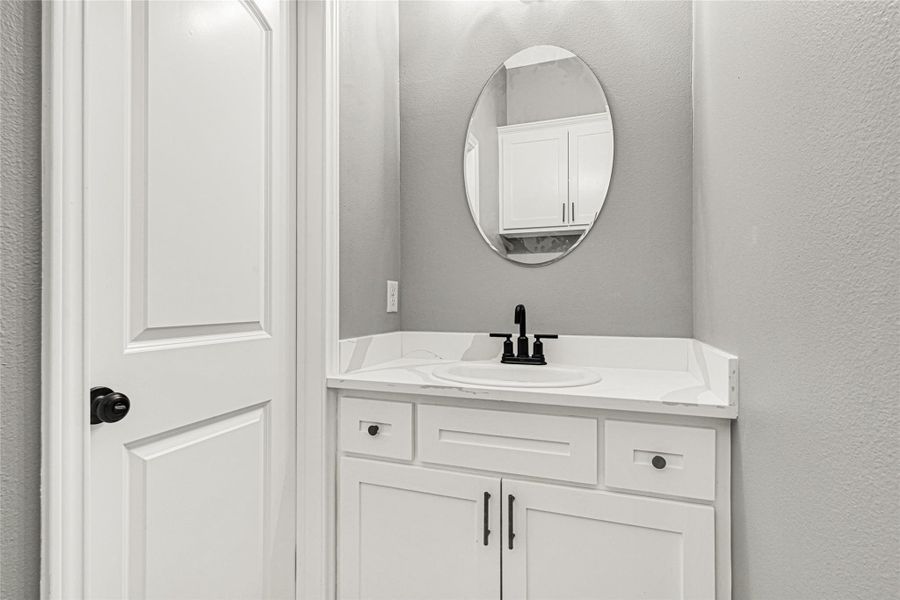 This is a compact, modern half bathroom with a sleek white vanity, an oval mirror, and black fixtures. The neutral gray walls and clean design offer a contemporary look.