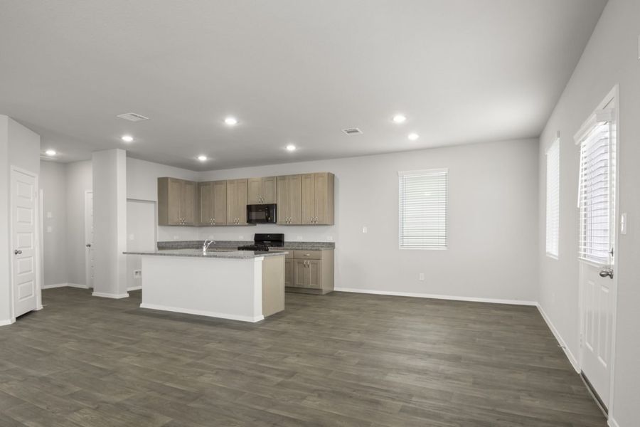 Image of a dining room with dark vinyl flooring and grey walls, and a L-shaped kitchen to the left