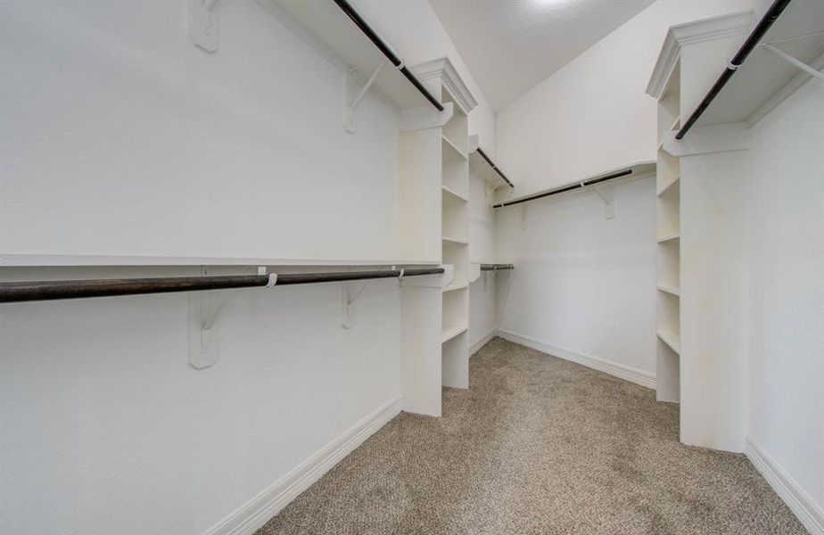 This is a spacious, well-organized walk-in closet with built-in shelving and multiple hanging rods, featuring carpeted flooring and a clean, neutral color scheme.