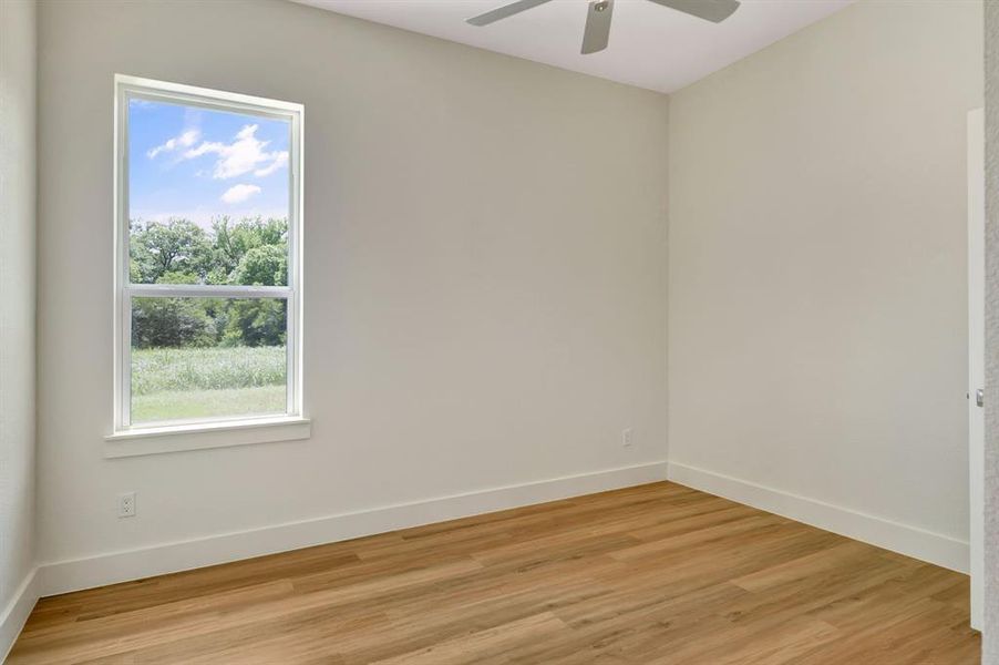 Bright interior space featuring a window with exterior scenery, wood-finish flooring, white baseboards, light-colored walls, and a ceiling fan Bright interior space featuring a window with exterior scenery, wood-finish flooring, white baseboards, light-colored walls, and a ceiling fan