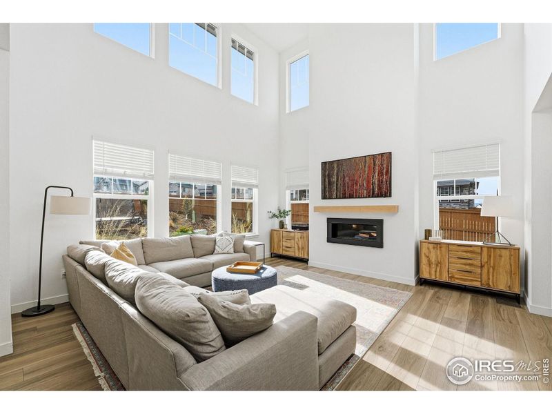 Two-story living room filled with natural light, anchored by a fireplace and open sightlines.