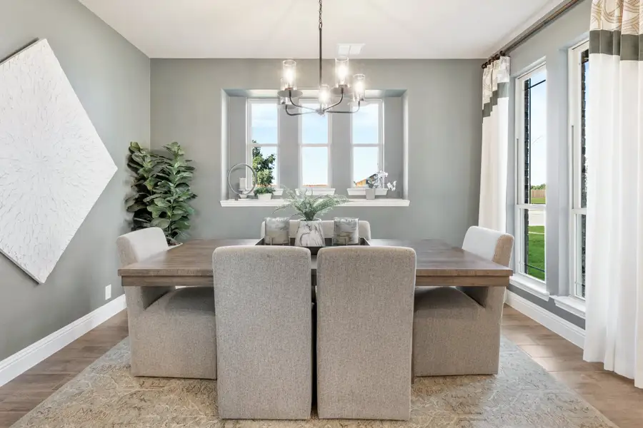 Dining room with wood table, upholstered chairs, chandelier, and large windows with natural light