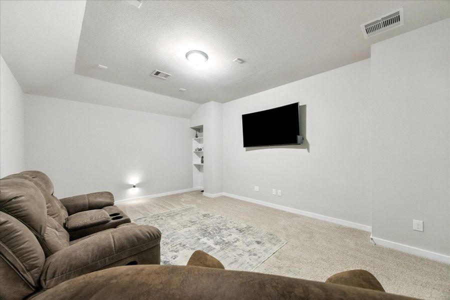 Bright and spacious media room featuring neutral carpeting, a large flat-screen TV mounted on the wall, and a cozy sectional sofa. Bright and spacious media room featuring neutral carpeting, a large flat-screen TV mounted on the wall, and a cozy sectional sofa.