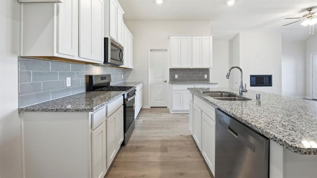 Kitchen featuring an island with a stainless steel sink, granite countertops, white cabinetry, a gray subway tile backsplash, and wood-finish flooring