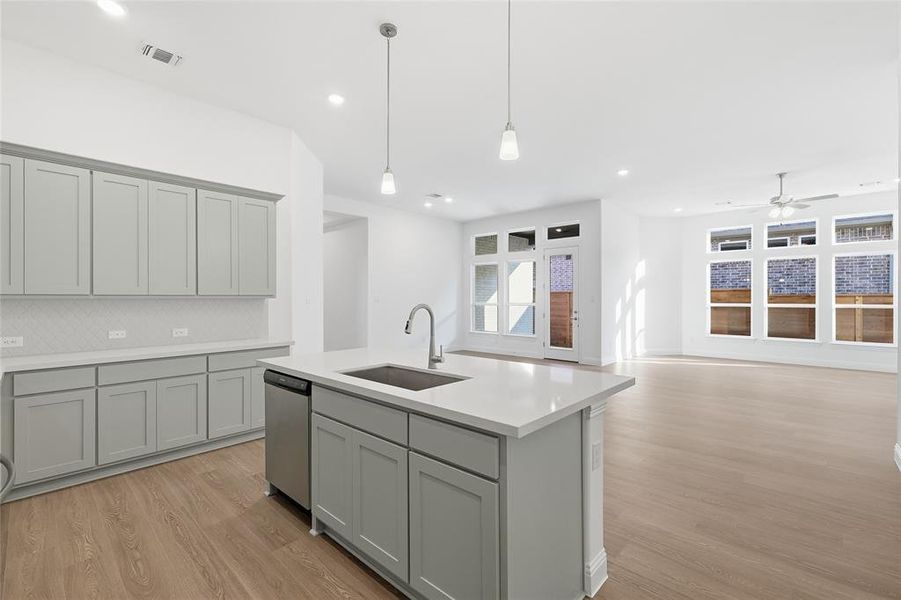 Kitchen with gray cabinets, light wood-style floors, pendant lighting, ceiling fan, and a center island with sink